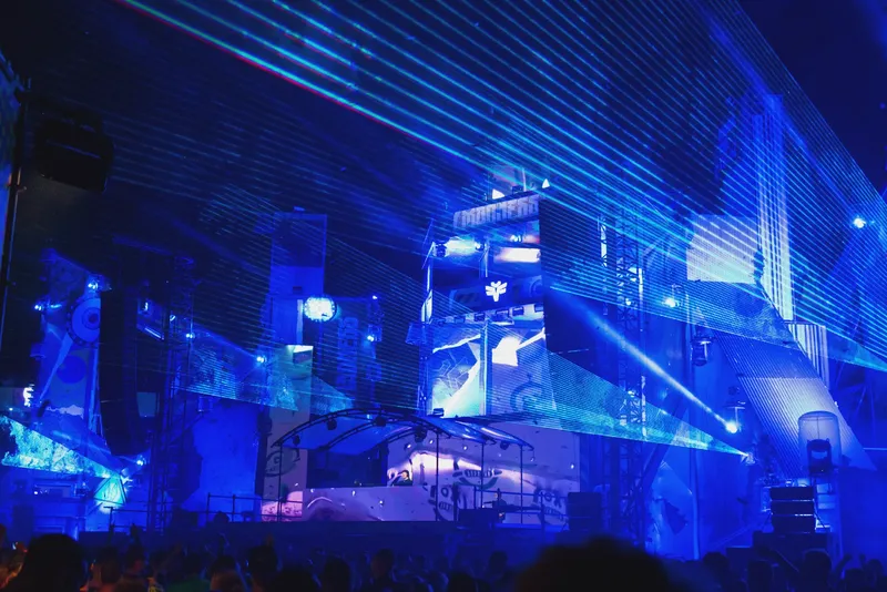 Spektakuläre Konzertbühne mit futuristischem Lichtdesign in intensiven Blautönen, modernster Laser-Show und beeindruckender visueller Inszenierung. Ein atmosphärisches Highlight der elektronischen Musikszene mit hochwertigem Produktionsdesign und energiegeladener Festival-Atmosphäre.
