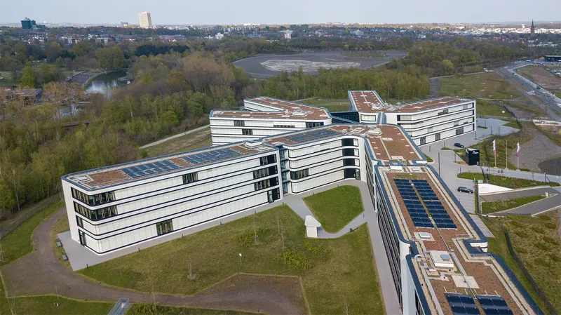 Amprion Hauptstelle: Innovative Architektur trifft Nachhaltigkeit - Moderner X-förmiger Gebäudekomplex mit Solarpanelen, eingebettet in grüne Parklandschaft. Luftaufnahme des energieeffizienten Hauptsitzes eines führenden Stromnetzbetreibers.
