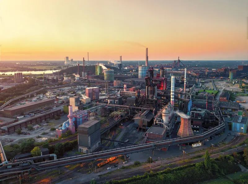 Atemberaubende Luftaufnahme der ThyssenKrupp Hochöfen in Duisburg bei Sonnenuntergang. Industriekultur im Ruhrgebiet mit imposanten Stahlwerken, Kühltürmen und Industrieanlagen vor goldenem Abendhimmel. Authentische Industriefotografie zeigt das Herz der deutschen Stahlindustrie.

