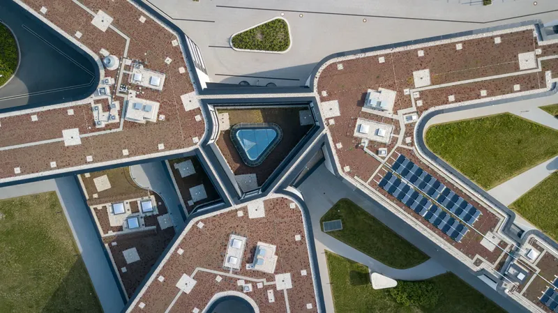 Exklusive Luftaufnahme der Amprion Hauptgeschäftsstelle mit innovativem Glasdach, dreieckigem Dachpool und nachhaltiger Architektur. Moderne Industriearchitektur vereint mit grünen Dachflächen und Solarenergie-Elementen zeigt zukunftsweisende Unternehmenskultur.
