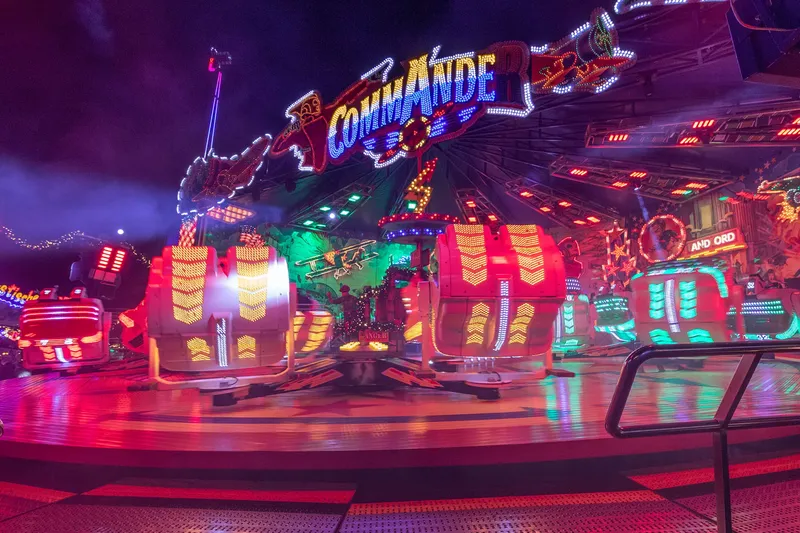 Spektakuläre Nachtaufnahme des Commander-Fahrgeschäfts auf der Cranger Kirmes mit beeindruckender LED-Beleuchtung in leuchtenden Farben. Ein stimmungsvolles Highlight des größten Volksfests im Ruhrgebiet, das die pure Kirmes-Atmosphäre einfängt.

